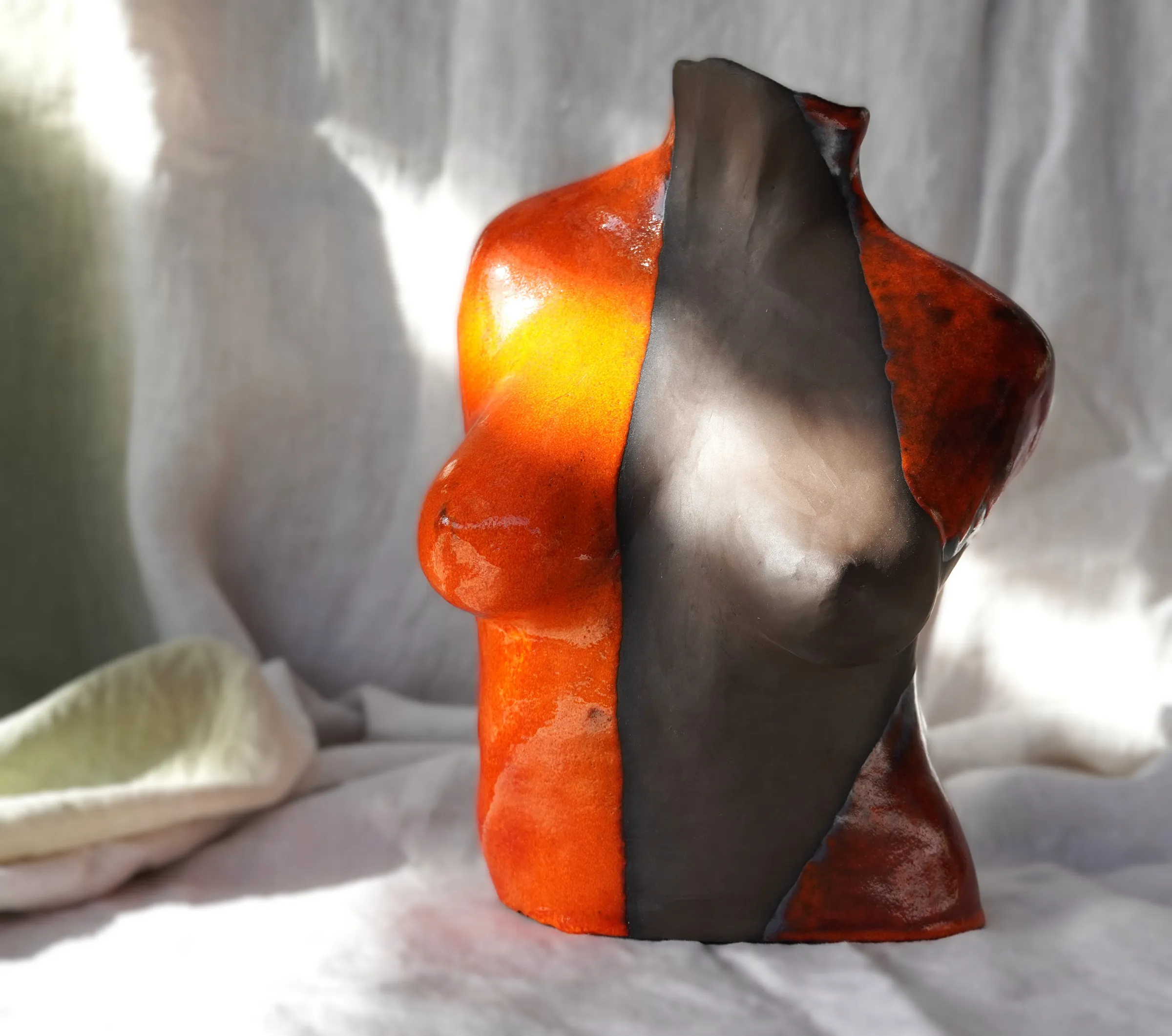Buste féminine en argile coloré en orange et noir, reflétant le soleil